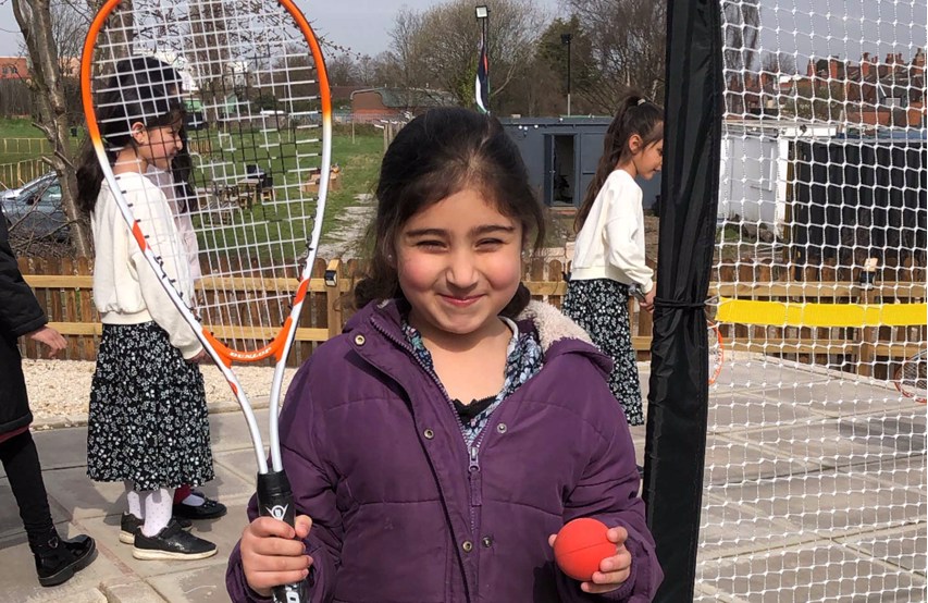 A girl holding up a squash racket and ball smiling